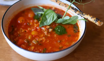Bol de minestrone italien fumant, garni de haricots blancs, légumes et petites pâtes, parsemé de parmesan râpé et de basilic