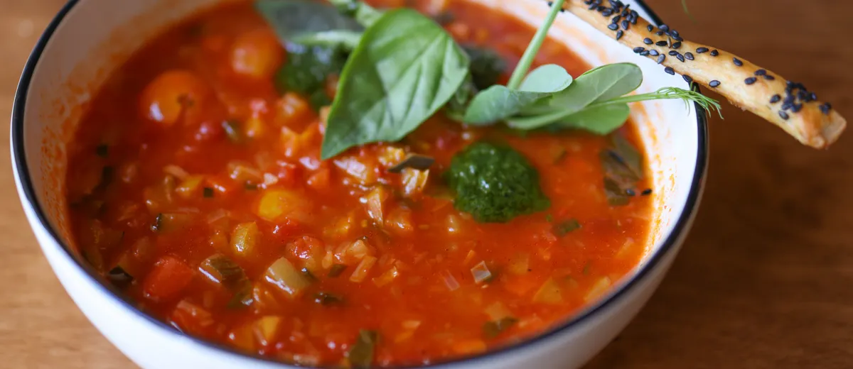 Bol de minestrone italien fumant, garni de haricots blancs, légumes et petites pâtes, parsemé de parmesan râpé et de basilic