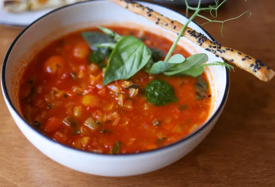 Bol de minestrone italien fumant, garni de haricots blancs, légumes et petites pâtes, parsemé de parmesan râpé et de basilic