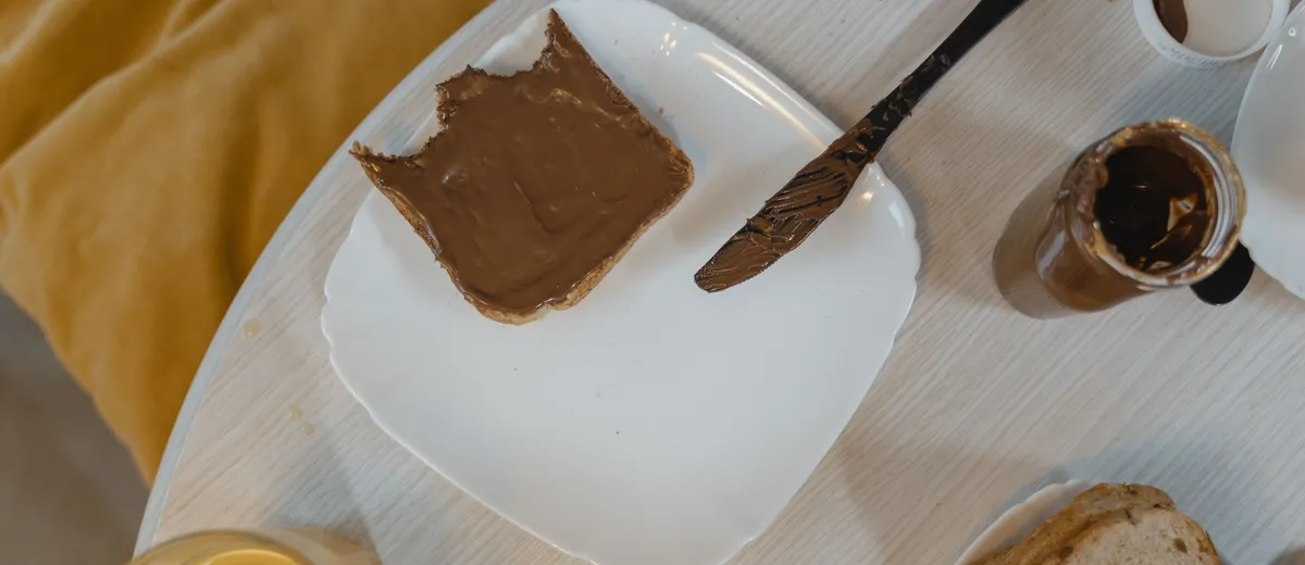 Pot de pâte à tartiner maison au chocolat et à la noisette, texture lisse et brillante, cuillère plongée dedans