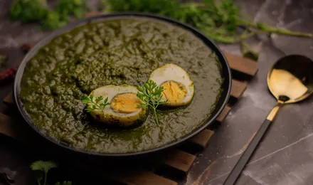 Palak paneer, cubes de fromage indien dans une sauce d'épinards vert profond parsemée de crème, servi avec du naan