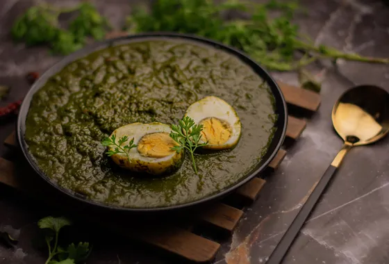 Palak paneer, cubes de fromage indien dans une sauce d'épinards vert profond parsemée de crème, servi avec du naan