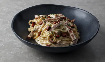 Spaghetti alla carbonara nappés d'une crème d'œuf et de pecorino, parsemés de guanciale croustillant et de poivre noir concassé.