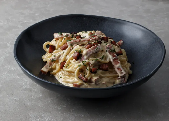 Spaghetti alla carbonara nappés d'une crème d'œuf et de pecorino, parsemés de guanciale croustillant et de poivre noir concassé.