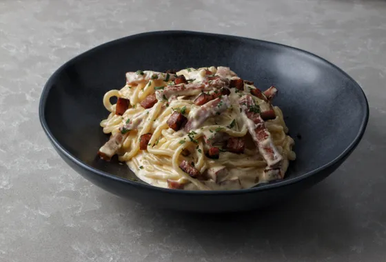 Spaghetti alla carbonara nappés d'une crème d'œuf et de pecorino, parsemés de guanciale croustillant et de poivre noir concassé.