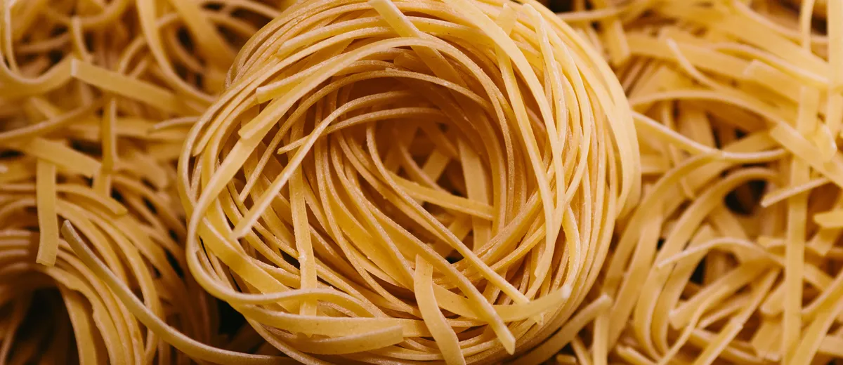 Nids de tagliatelles fraîches maison farinées, posés sur un plan de travail en bois