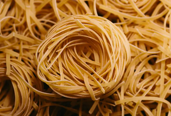 Nids de tagliatelles fraîches maison farinées, posés sur un plan de travail en bois