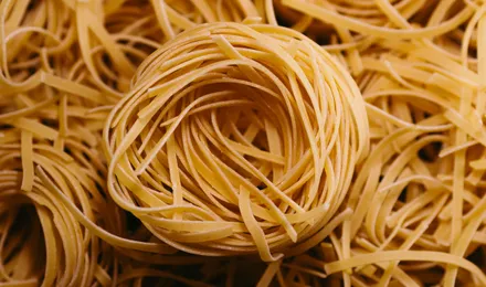 Nids de tagliatelles fraîches maison farinées, posés sur un plan de travail en bois