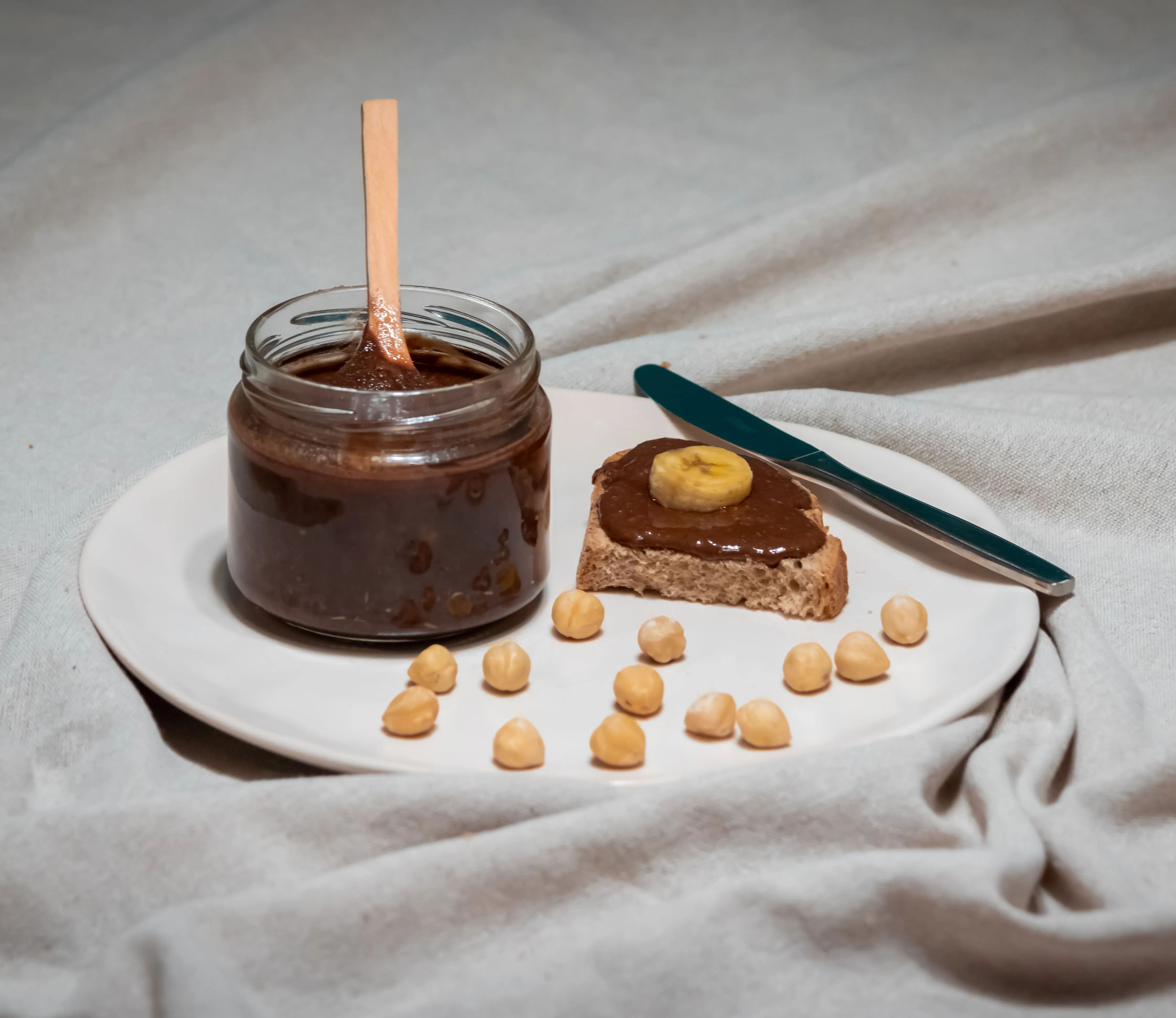 Bocal de pâte à tartiner chocolat-noisette maison avec une cuillère et des noisettes entières autour
