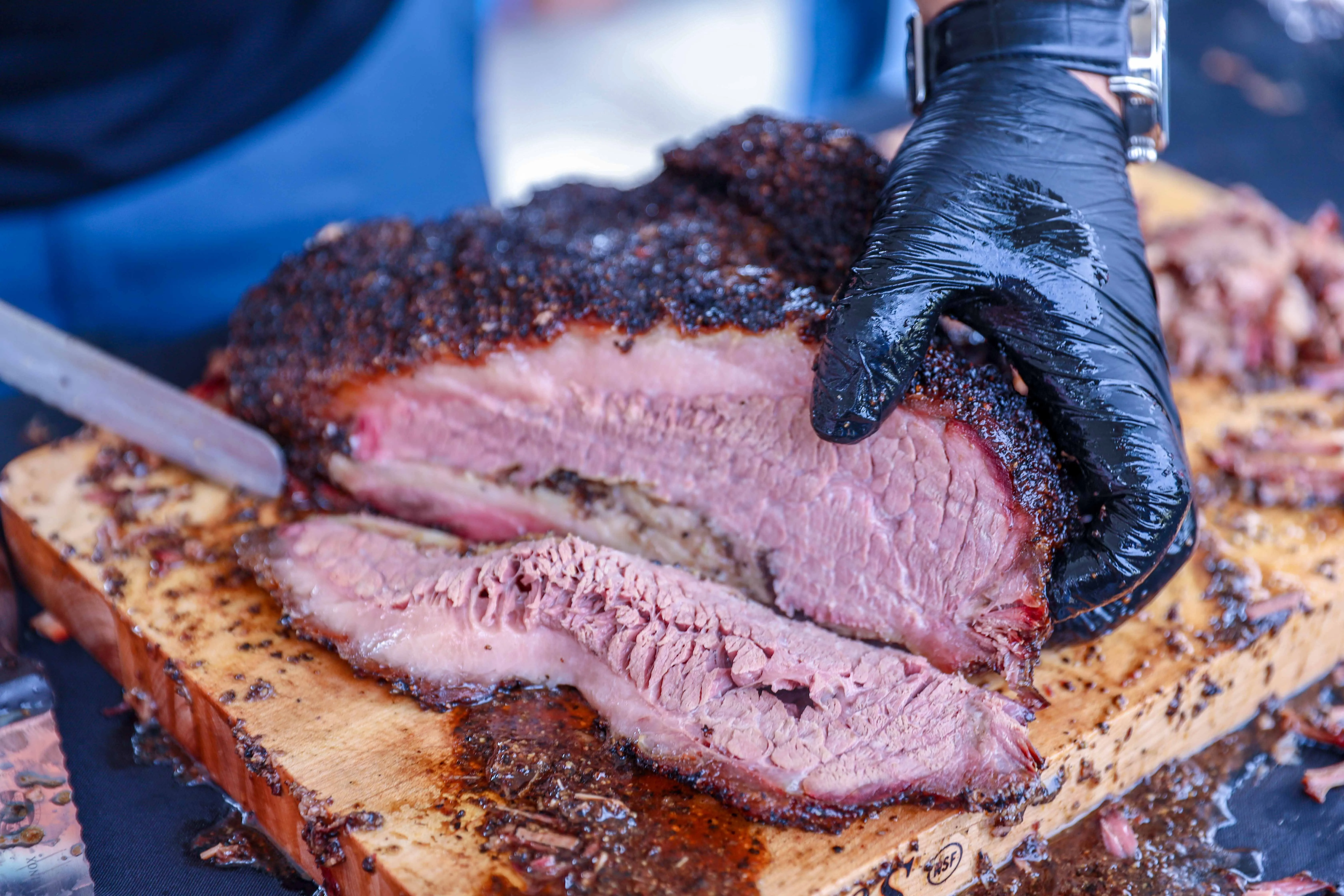 Tranches de brisket fumée à la texane sur une planche en bois, croûte poivrée noire et anneau de fumée rose visibles