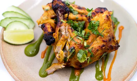Poulet tandoori, cuisses rôties rouge orangé légèrement charbonnées avec quartiers de citron et rondelles d'oignon