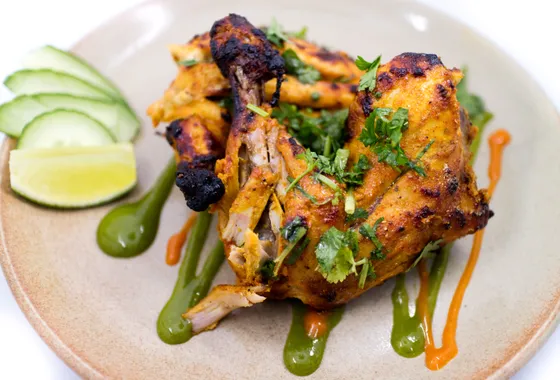 Poulet tandoori, cuisses rôties rouge orangé légèrement charbonnées avec quartiers de citron et rondelles d'oignon