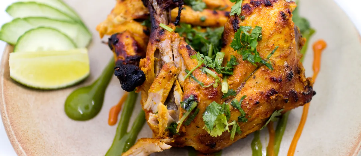Poulet tandoori, cuisses rôties rouge orangé légèrement charbonnées avec quartiers de citron et rondelles d'oignon