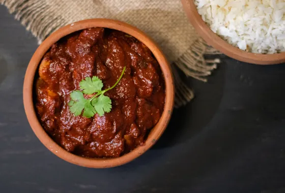 Poulet vindaloo, curry goanais rouge profond parsemé de coriandre, servi avec du riz basmati