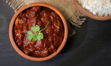 Poulet vindaloo, curry goanais rouge profond parsemé de coriandre, servi avec du riz basmati