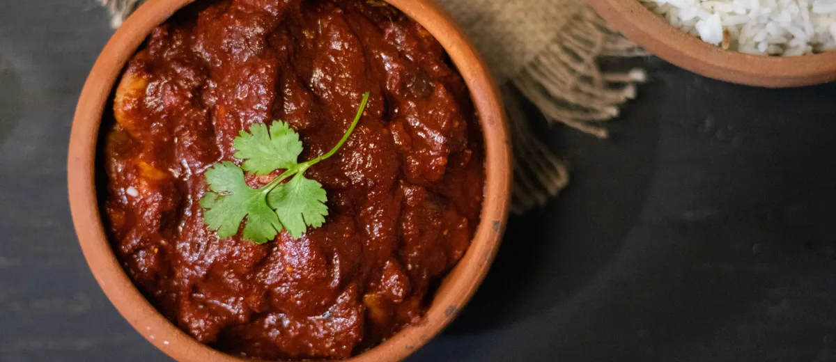 Poulet vindaloo, curry goanais rouge profond parsemé de coriandre, servi avec du riz basmati