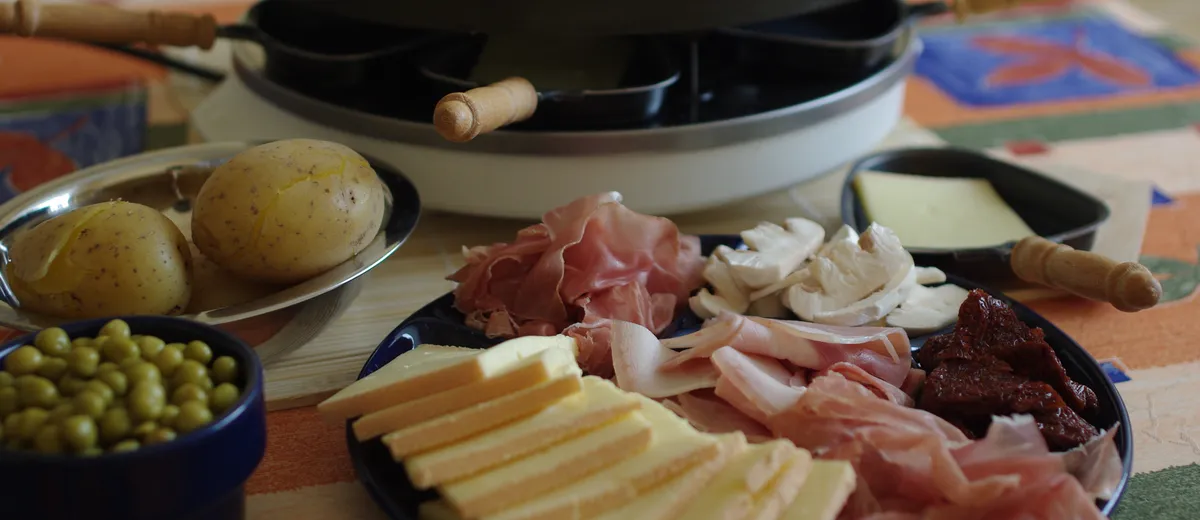 Table de raclette avec fromage fondu coulant sur des pommes de terre, charcuteries et cornichons