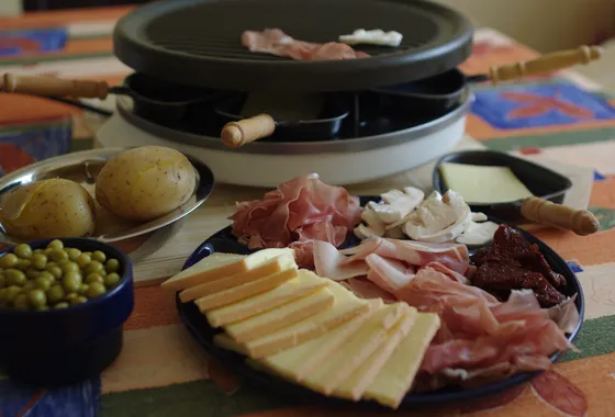 Table de raclette avec fromage fondu coulant sur des pommes de terre, charcuteries et cornichons