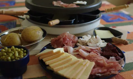 Table de raclette avec fromage fondu coulant sur des pommes de terre, charcuteries et cornichons