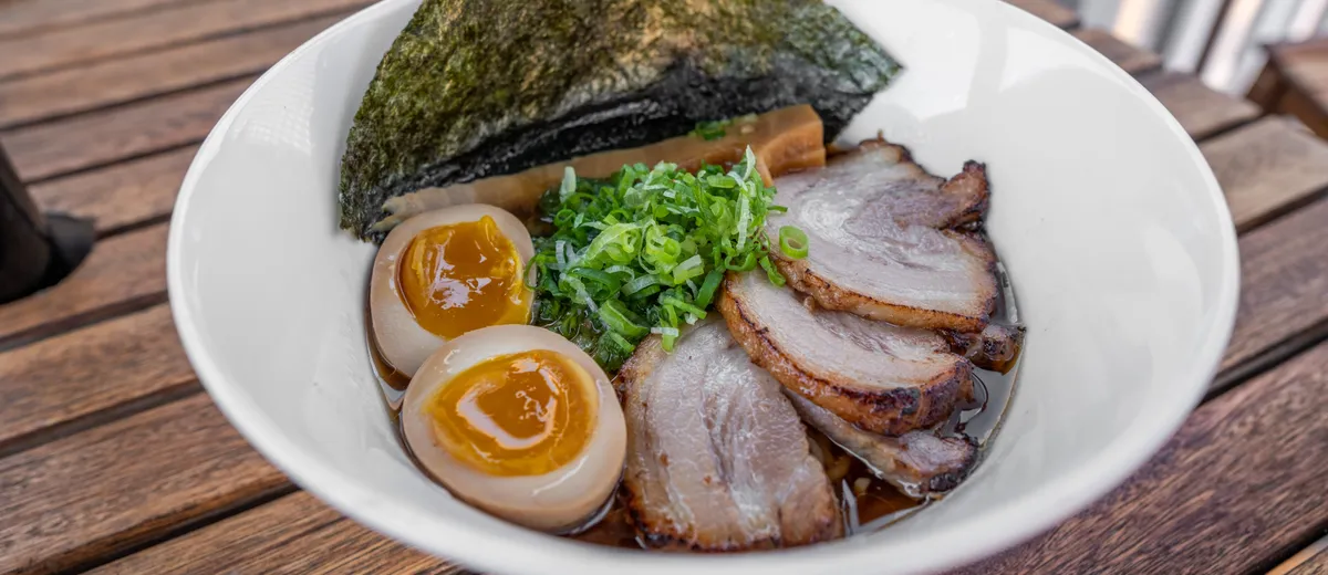 Ramen shoyu dans un bol large : nouilles, tranches de chashu, demi-œuf mariné au jaune coulant, nori et oignon vert dans un bouillon ambré.