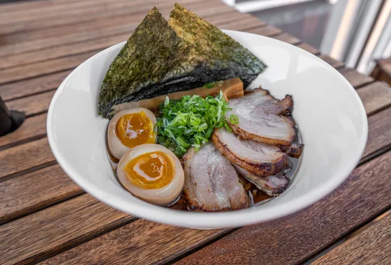 Ramen shoyu dans un bol large : nouilles, tranches de chashu, demi-œuf mariné au jaune coulant, nori et oignon vert dans un bouillon ambré.