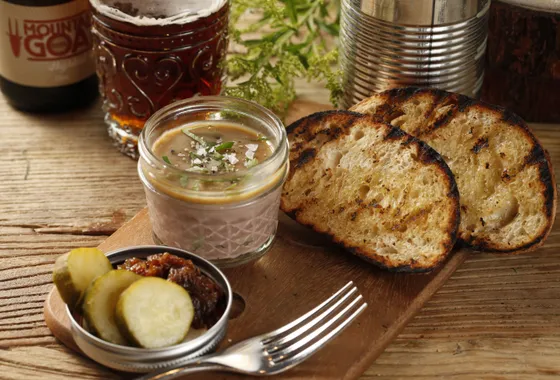 Rillettes du Mans dans un pot en grès, chair de porc effilochée en gros filaments dorés sous une couche de graisse, servies avec du pain de campagne et des cornichons