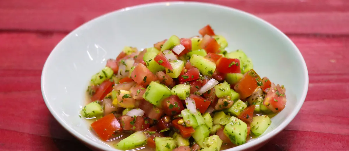 Salade Shirazi en petits dés de concombre, tomate et oignon rouge, parsemée de menthe séchée dans un bol en céramique