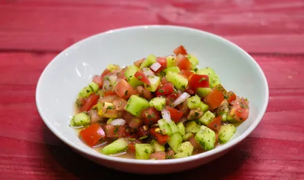 Salade Shirazi en petits dés de concombre, tomate et oignon rouge, parsemée de menthe séchée dans un bol en céramique