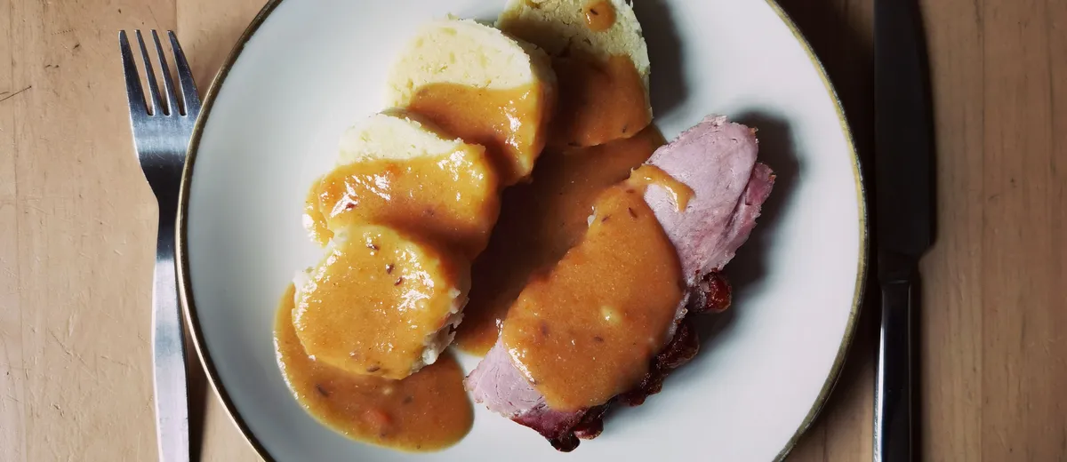 Sauerbraten tranché, rôti de bœuf allemand nappé d'une sauce brune brillante, accompagné de chou rouge et de knödel.