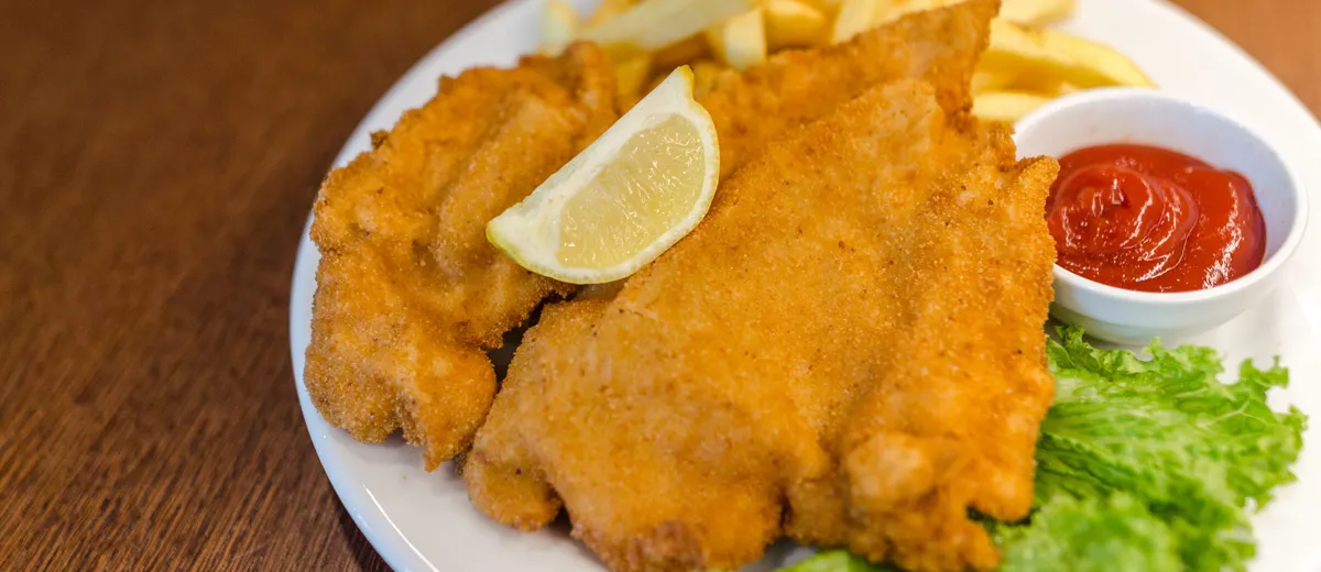 Schnitzel de porc pané et doré, servi avec un quartier de citron et des pommes de terre au persil