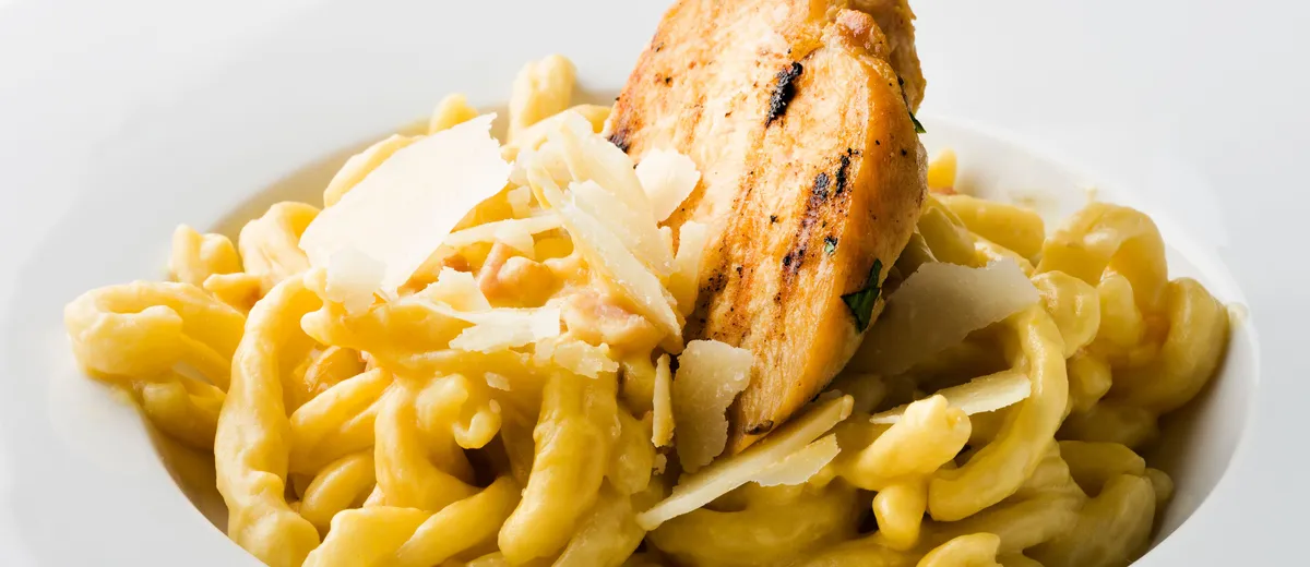 Spätzle maison dorés au beurre dans une poêle, parsemés de persil
