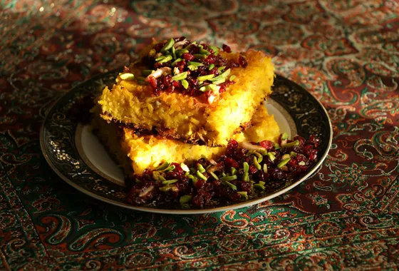 Tahchin démoulé, gâteau de riz safrané doré et croustillant garni de poulet effiloché et d'épines-vinettes rouges.