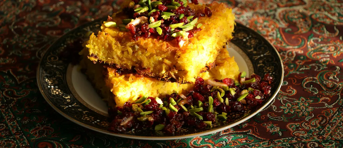 Tahchin démoulé, gâteau de riz safrané doré et croustillant garni de poulet effiloché et d'épines-vinettes rouges.