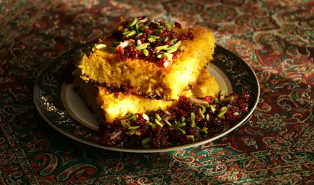 Tahchin démoulé, gâteau de riz safrané doré et croustillant garni de poulet effiloché et d'épines-vinettes rouges.