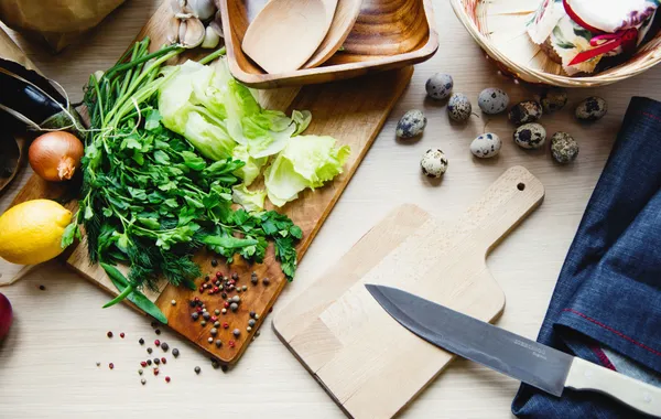 Couteau de chef, planche en bois, poêle et économe posés sur un plan de travail clair