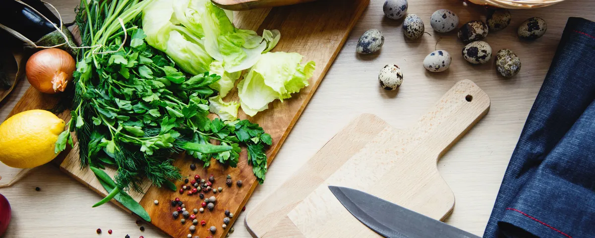 Couteau de chef, planche en bois, poêle et économe posés sur un plan de travail clair